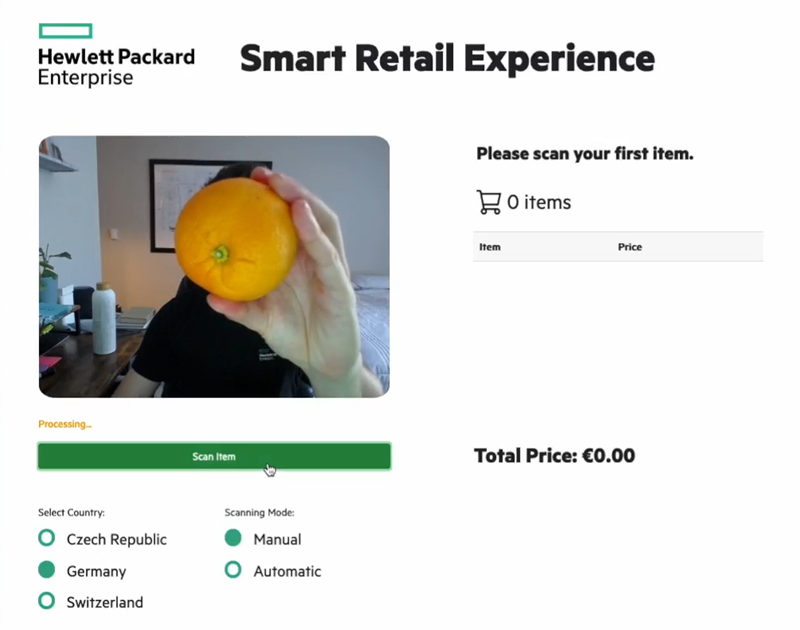 Leveraging the served model, the smart retail application can identify fresh produce through a connected webcam and clean user interface. This pictures shows a human presenting an orange to a checkout webcam.